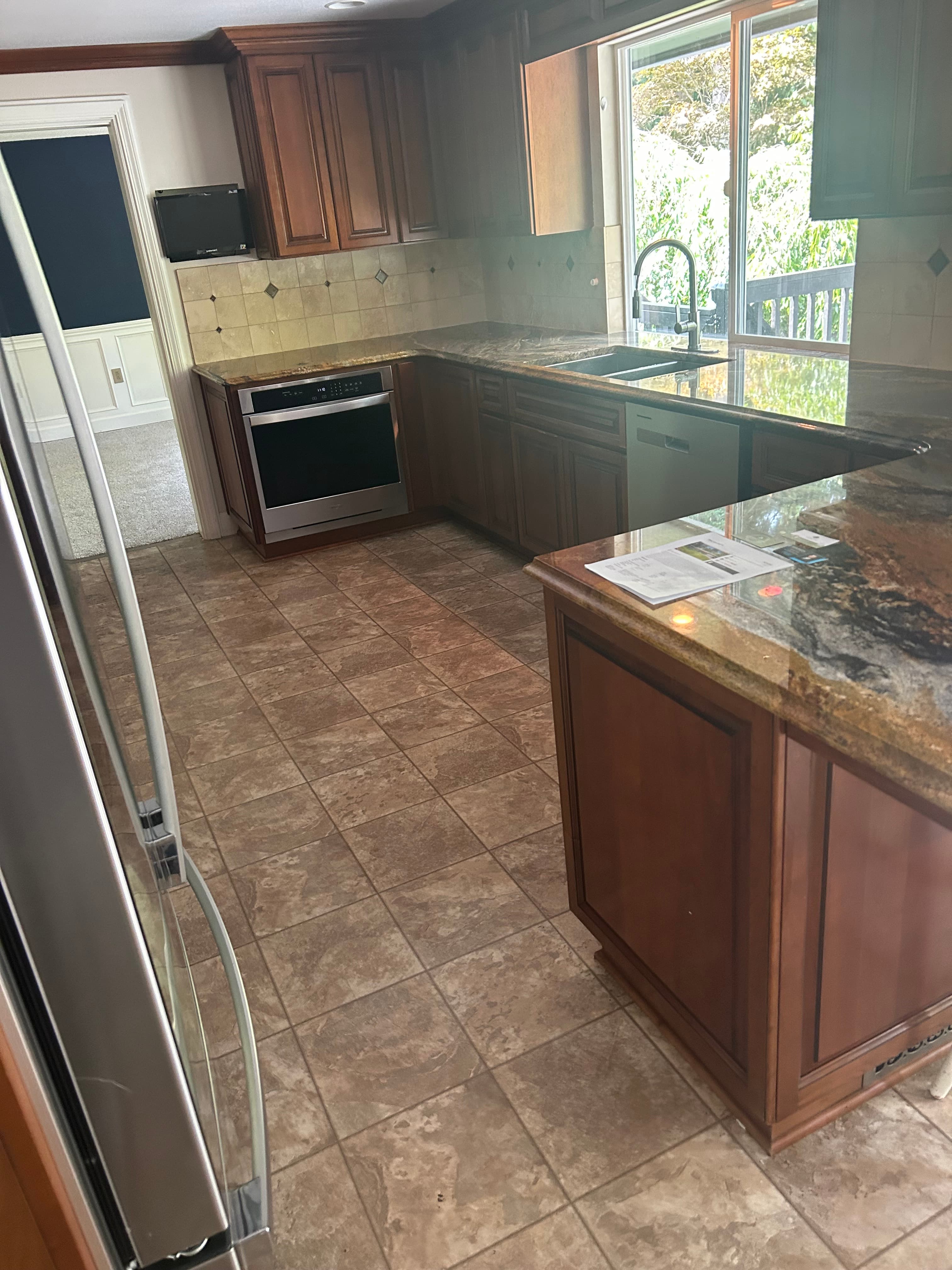 Traditional kitchen featuring brown wood cabinets, granite countertops, tile flooring, and stainless steel appliances.